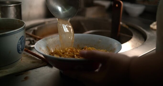 Hawker Pouring Hot Soup Broth Into Bowl of Noodles