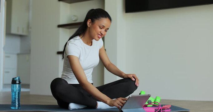Online video tutorial while virtual training at home. Workout at home in living room, viewing online training on tablet.