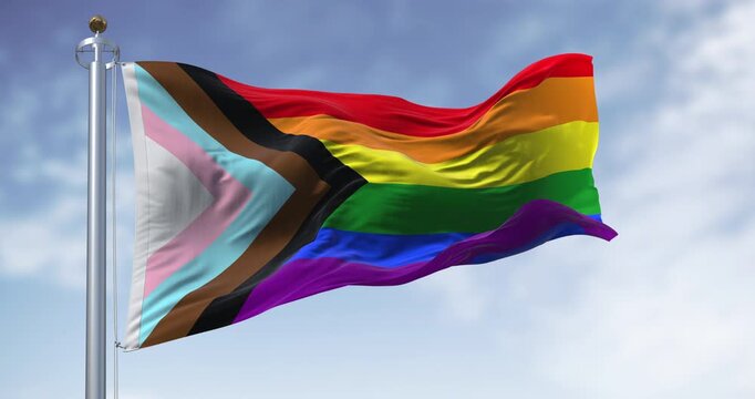 Progress Pride Flag Waving on Flagpole Against Blue Sky