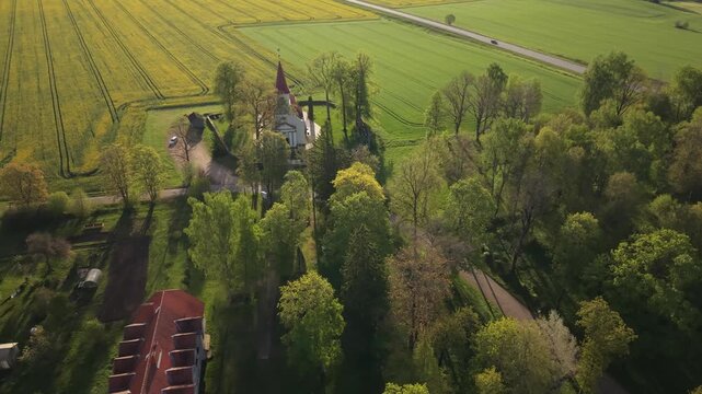 Aerial view of a quaint church surrounded by vibrant rapeseed fields and lush greenery, showcasing the picturesque landscape and rural charm of the countryside in springtime