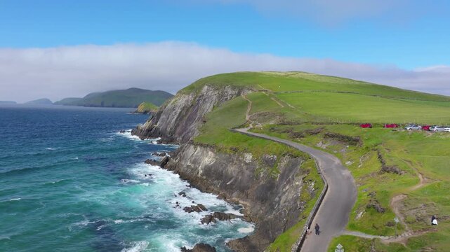 A winding road hugs the rugged coastline, bordered by vibrant blue waters and lush green hills. Perfect for travel documentaries or scenic drives.