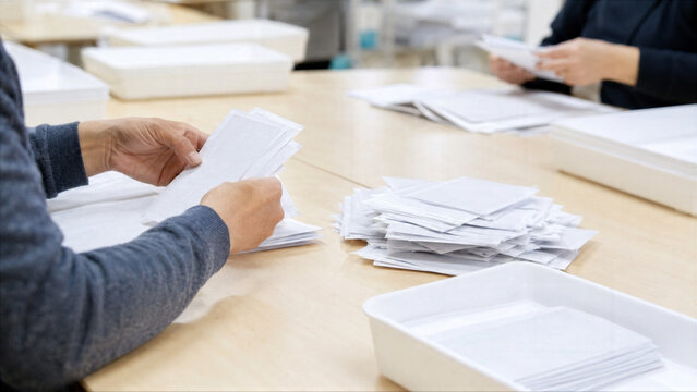 Election officials counting paper ballots after voting. Woman and man sorting envelopes at polling station during election day. Democracy process, civic duty and political voting concept.