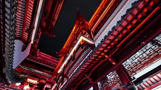 Red-lit traditional Chinese buildings rise against a dark sky, showcasing intricate architectural details. Ideal for cultural documentaries or travel features.
