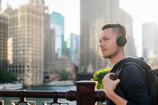 Portrait of mid adult man with headphones walking on waterfront in downtown Chicago during day. Urban lifestyle, modern audio technology, city music streaming and wellness concept.