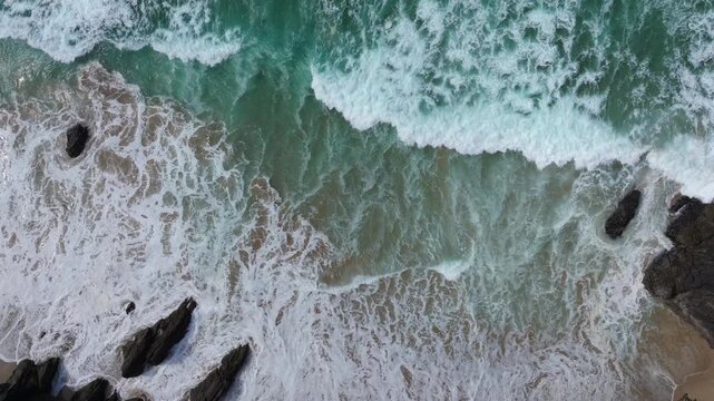 Waves cascade over rocks and sandy beach at Coumeenoole, creating dynamic patterns. Ideal for projects focused on coastal landscapes or oceanic themes.