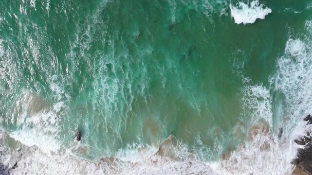 Waves create intricate patterns as they meet the sandy shore and rocks along the Irish coast. Captures the dynamic motion of the ocean, ideal for coastal or nature themes.