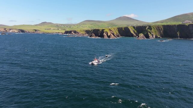A boat moves steadily across the open sea, framed by the rugged cliffs and rolling green hills of Ireland. Suitable for travel documentaries or maritime-themed content.