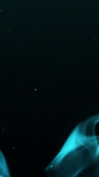 Vertical Elegant Wisps of Blue Smoke and Particles Against Black Background