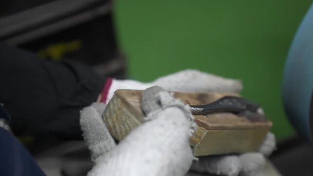 Close-up of assembled pliers held in wooden jig being polished on grinding wheel