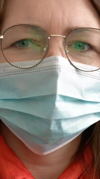 A woman wears a mask as she looks directly at the camera. The woman's glasses and expression convey a serious tone in a close-up setting.