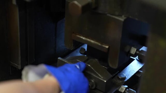 Worker wearing blue gloves operating press machine to stamp pliers jaw teeth pattern