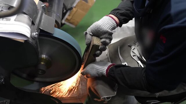 Worker grinding assembled pliers on bench grinder with wooden holding jig for precision edge