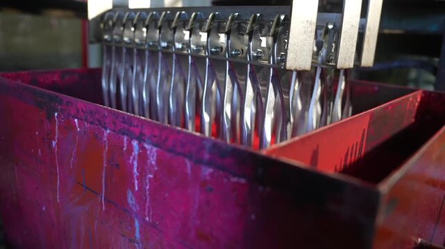 Rows of finished pliers suspended above red collection container after electroplating process