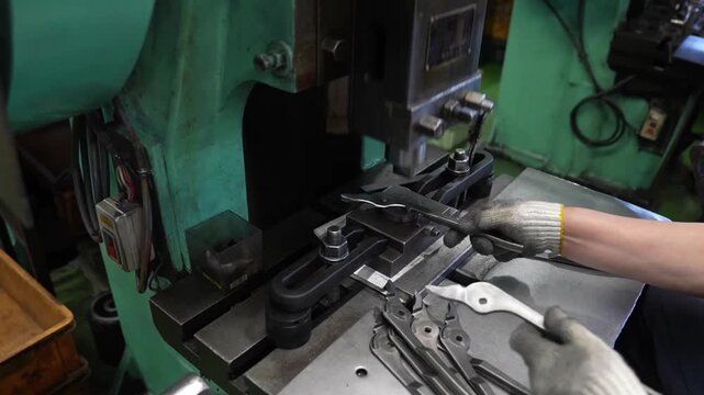 Worker pressing pliers blanks through mechanical stamping die on green industrial press machine