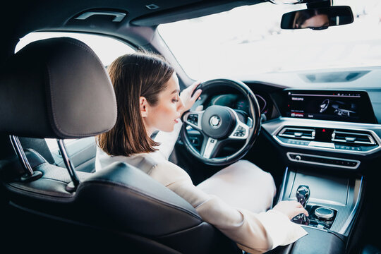 Woman driving a luxury car interior with modern dashboard and touchscreen controls, professional driver adjusting gearshift and steering wheel while commuting or testing a high-end vehicle