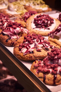 A pastry display case viewed from the outside, filled with delicious sweets and illuminated by warm lighting.
