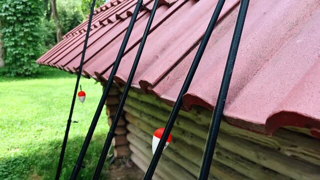 Black fishing rods leaning against a wooden cabin with a red tile roof