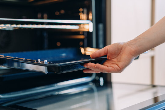 Woman remove baking tray from oven in modern kitchen