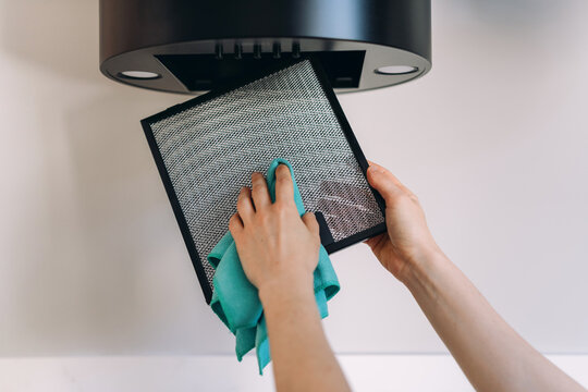 Woman cleaning removable filter from kitchen extractor hood appliance