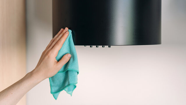 Woman cleaning kitchen hood appliance with cloth