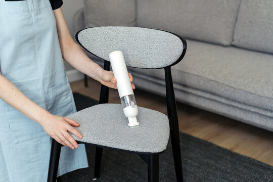Woman uses cordless vacuum cleaner on chair in living room