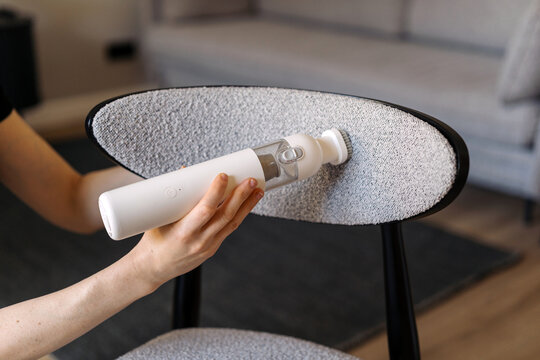 Woman uses cordless vacuum cleaner to tidy chair at home