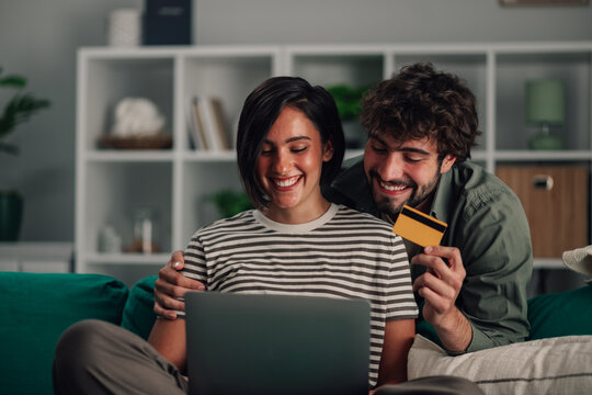 Happy couple shopping online together from home using laptop and credit card for e commerce purchases