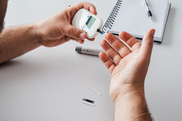Fototapeta premium Close-up of a mature man's hands using a lancet and glucometer for a finger-prick blood sugar test at a table illustrating diabetes self-monitoring and home healthcare.