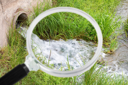 SEWAGE WATER DISCHARGING FROM A DRAIN PIPE INTO A STREAM WITH A MAGNIFIER HIGHLIGHTING CONTAMINATION - THIS ENVIRONMENTAL INSPECTION IMAGE ILLUSTRATES POLLUTION, WASTEWATER, DRAINAGE AND MONITORING