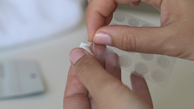 Female hands carefully peeling hydrocolloid acne patch before skincare application. Beauty and dermatology concept focused on acne prevention, clear skin and cosmetic selfcare routine.