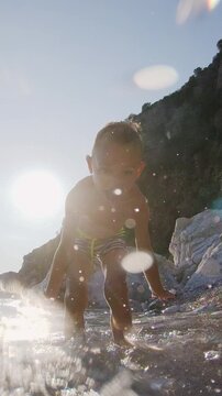 Cute small boy splashing water in slow motion on the beach. Caucasian 5 year old boy having fun on summer beach holiday at sunset