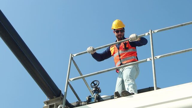 Male engineer with safety vest and helmet maintaining a cooling tower. Technician man trying to rotate the valve while checking building cooling system. A worker inspecting rooftop cooling tower.