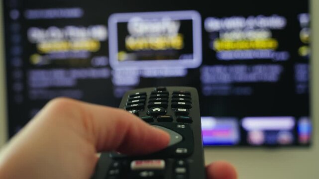 Close-up of a hand holding a remote control and changing channels on a smart TV. Home entertainment, television viewing and digital media concept. High quality 4k footage