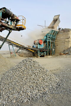 Crushed stone pile close up with industrial quarry rock crushing plant machine on background
