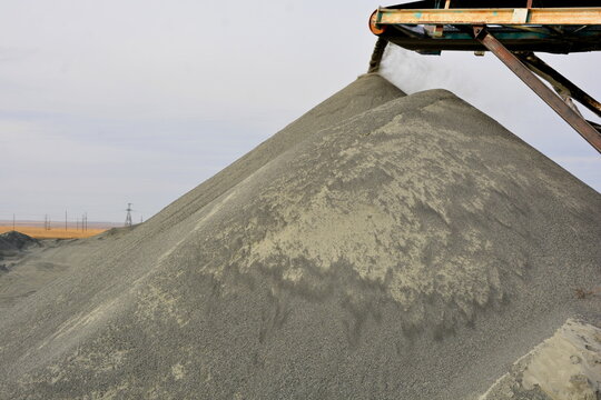 Large pile of grey crushed stone aggregate pouring from conveyor belt at industrial quarry plant