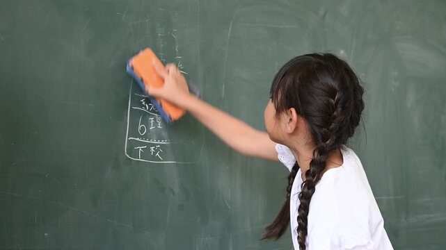 教室で笑顔で黒板を消す低学年の女子小学生