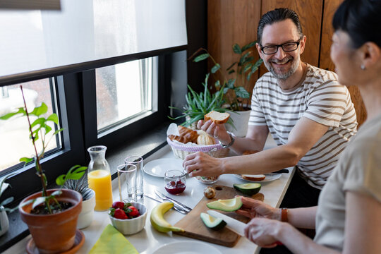 Cheerful couple talking in a bright kitchen while preparing refreshments. Authentic home moment highlighting communication, trust, emotional connection and modern family life