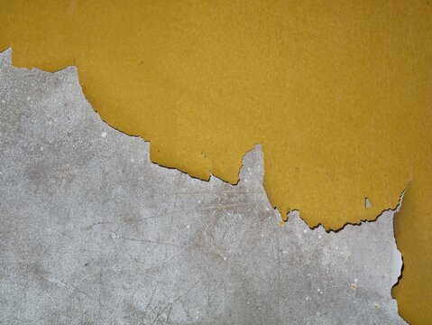 Close-up shot of vibrant yellow paint peeling and cracking off a weathered, textured gray concrete surface. Creating a rustic and gritty industrial texture perfect for background use