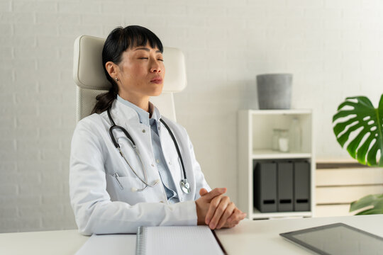 Female doctor practicing mindfulness and relaxation in clinic office. Healthcare wellbeing, stress management, resilience, self-care and mental wellness in the medical profession