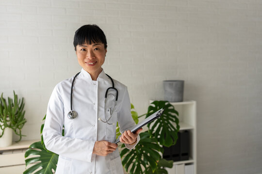 Female physician standing with clipboard in medical office. Healthcare management, patient consultation and professional medical services concept