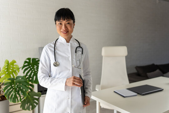 Professional female doctor posing in modern clinic with clipboard. Medical leadership, healthcare career, expertise and patient trust concept