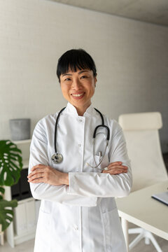 Confident smiling female doctor standing with arms crossed in modern clinic. Healthcare expertise, medical professionalism and patient trust concept