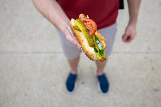 Close-up of hand holding traditional Chicago style hot dog on street city background. Fast food, american cuisine, street food culture and summer lunch concept.