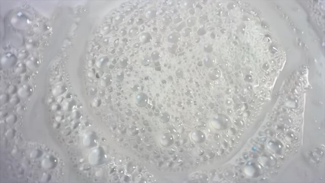 washing foam forming circular patterns top view as bubbles expand and burst while the camera rotates slowly, revealing surface tension behavior, liquid interaction and cleaning process texture