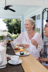 Senior in white lace top and female friend sitting at wooden table sharing tea and cupcakes © wavebreak3