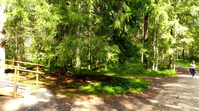 Two girls run through the summer forest near a small wooden house.