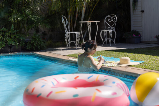 Donut-shaped inflatable float drifting on turquoise pool water near beach ball at patio, copy space