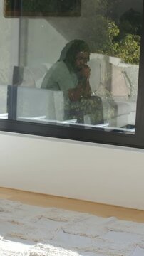 Vertical video: Glass glare drawing man on sofa in green top shifting hands to mouth and resettling
