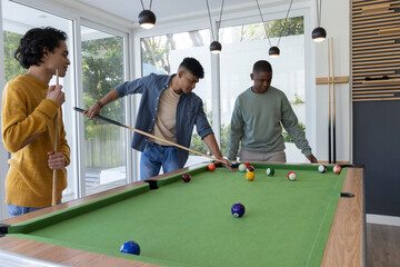 Obraz premium Diverse male friends playing pool on green-felt table in modern recreation room with cues