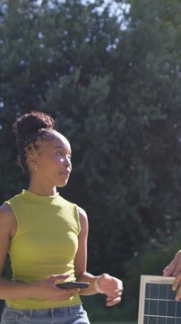 Vertical video: Joining left, woman lime top checking solar panel app, man steadying panel in yard